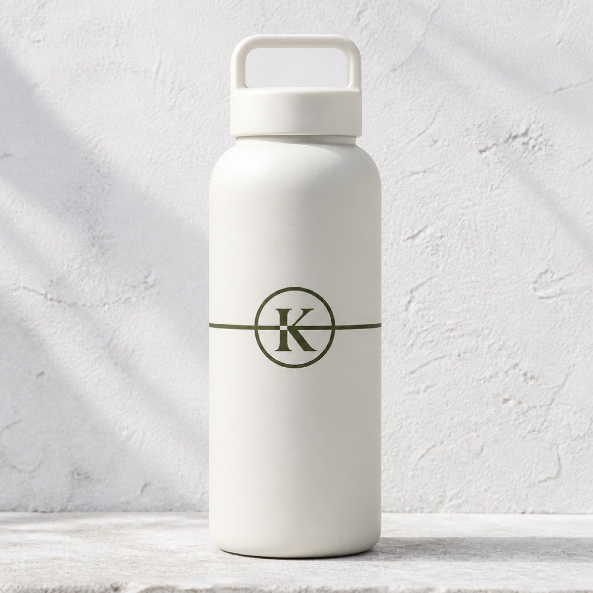 A matte cream Kinesis water bottle with a moulded carry handle, carrying the olive circled K monogram with the strike line running through it.