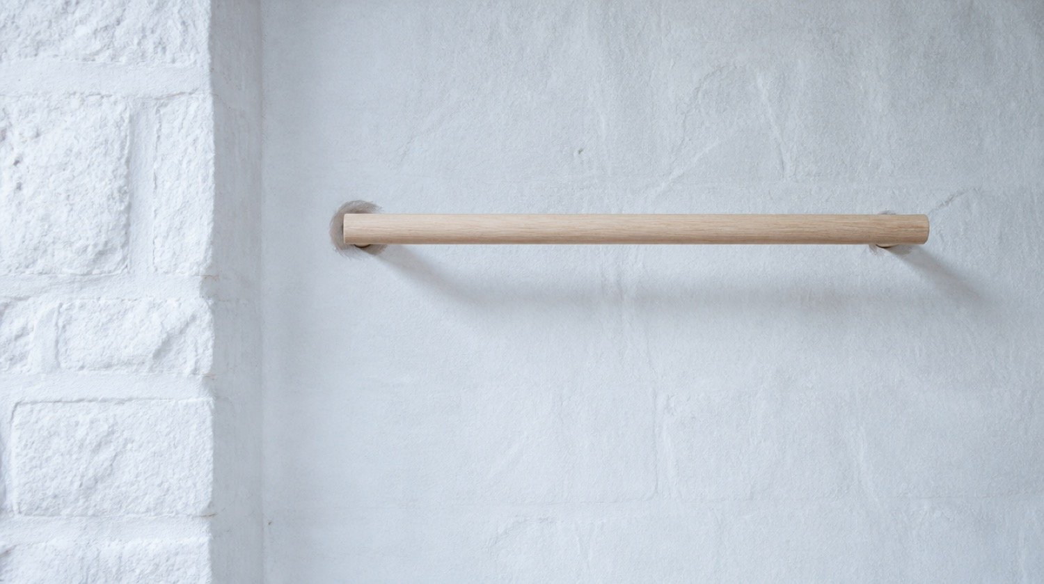 A wall-mounted wooden rail against a limewashed studio wall, styled as architecture rather than gym equipment.