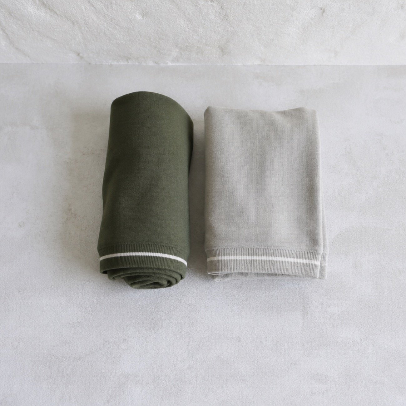 Rolled Kinesis textiles in olive and grey stacked on stone.