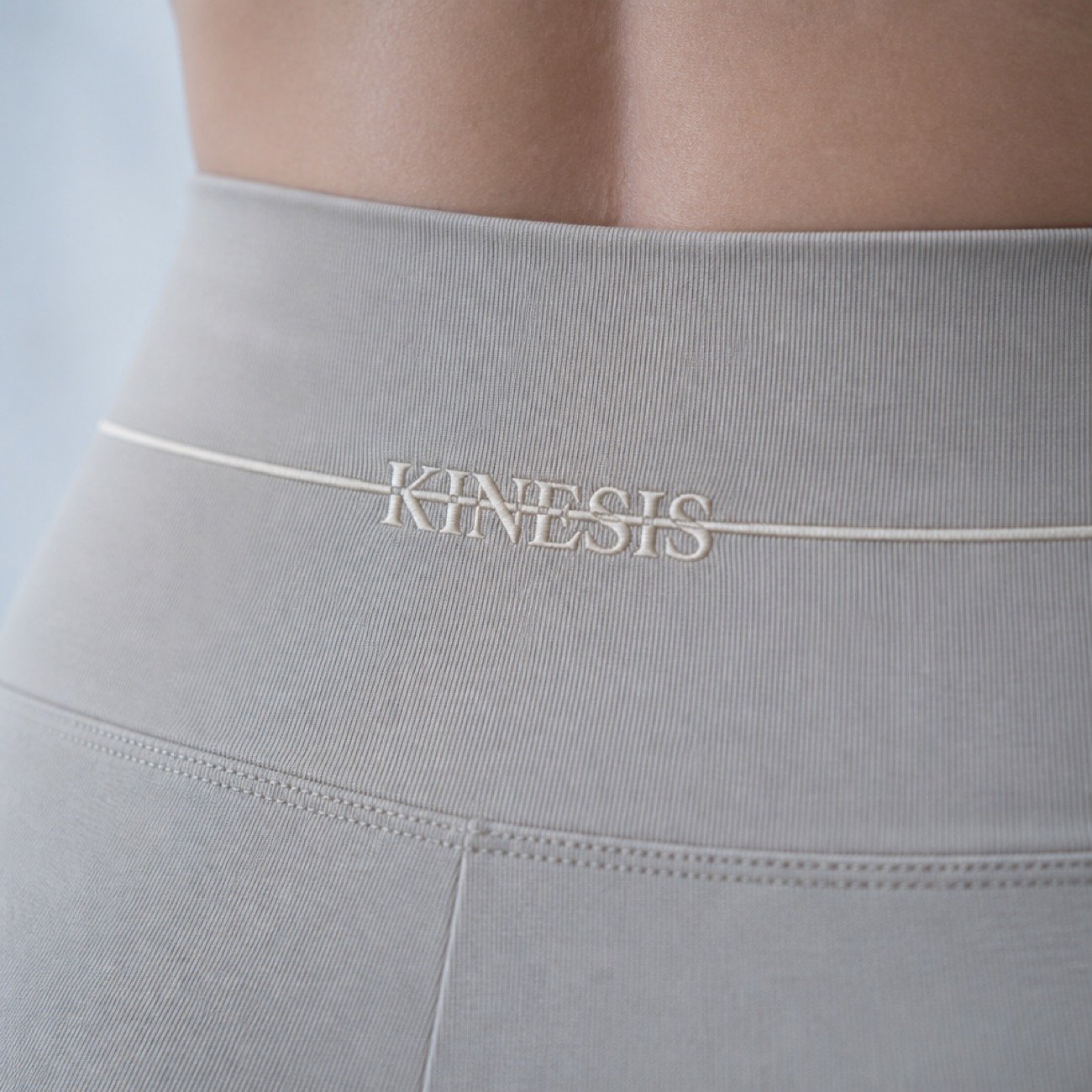 The Kinesis wordmark embroidered in cream across the waistband of grey leggings, the strike line running out to both seams.