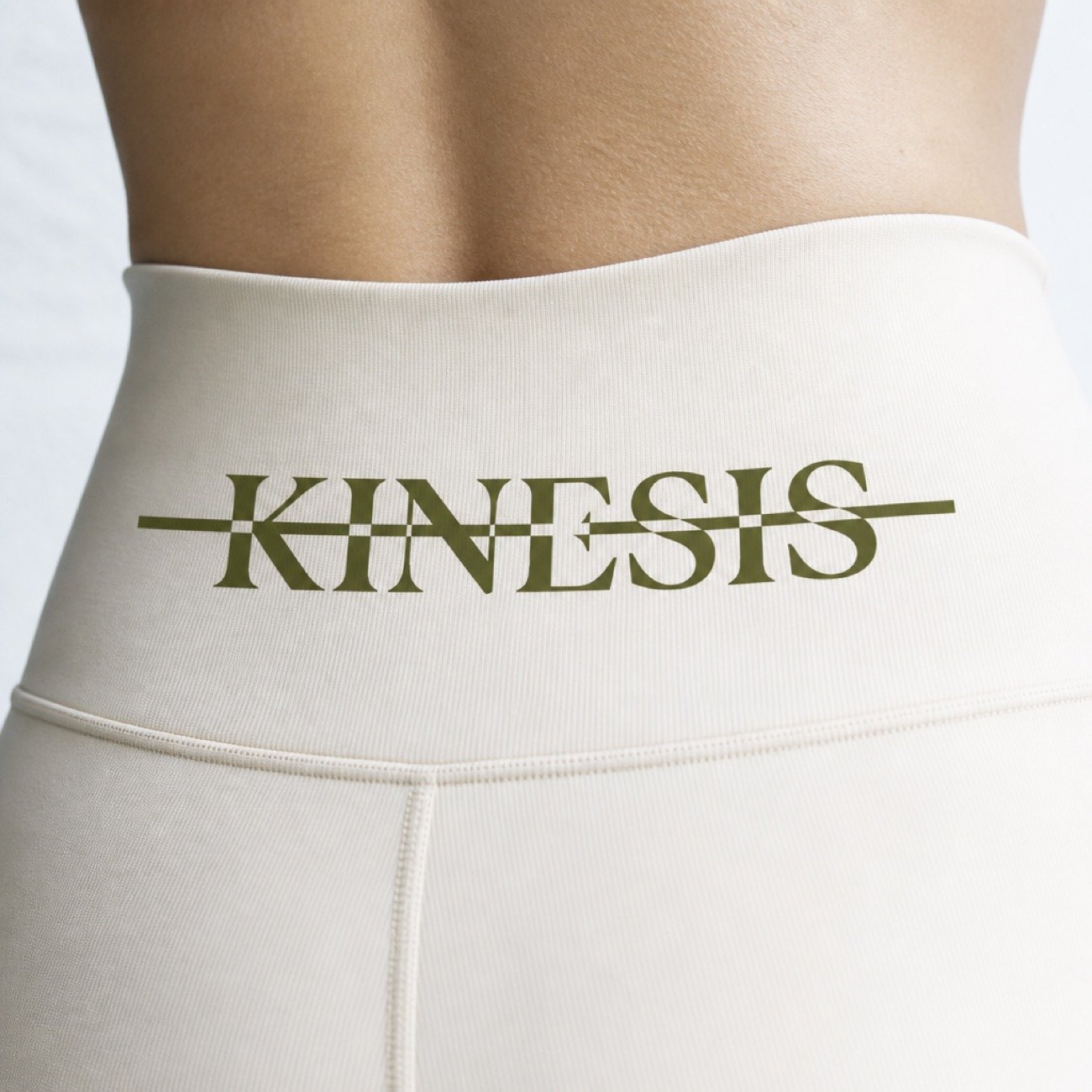 Close detail of the Kinesis wordmark and its strike line printed in olive on a cream legging waistband.